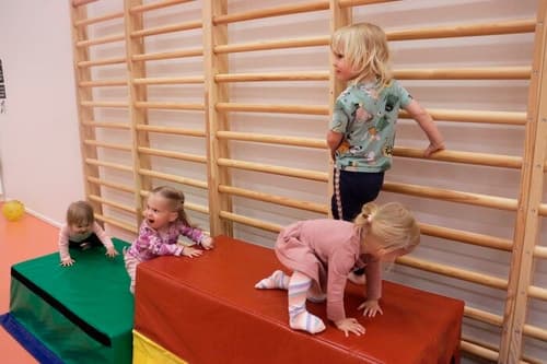 Kolme lasta kiipeilee erikokoisten patjojen päällä. Neljäs lapsi seisoo korkeimmalla patjalla.